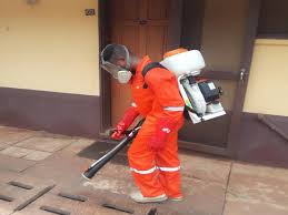 A man dressed in an overall spraying chemicals on the ground.