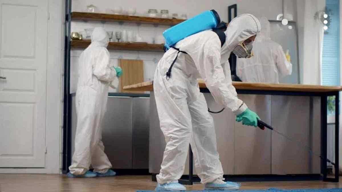 A man dressed in white overall spraying chemicals on the ground