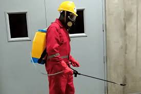 A man in a red overall spraying chemicals in a room